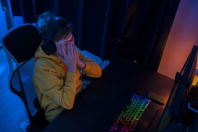 Exhausted boy with headphones sitting on chair while playing video game at home