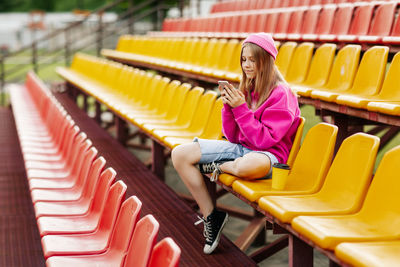 A teenage girl sits on the school bleachers and writes a message on her phone 