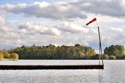 Red flag by lake against sky