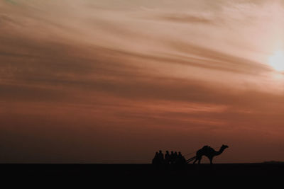 Silhouette people riding on beach against sky during sunset