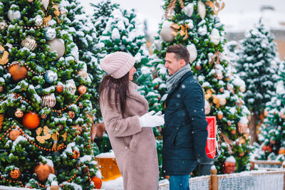 Side view of smiling couple standing by christmas tree outdoors in winter