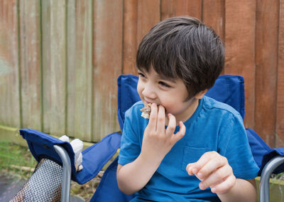 Boy looking away while sitting against blue wall