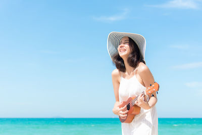 Young woman wearing hat against sea against sky