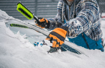 Midsection of man cleaning ice on windshield during winter