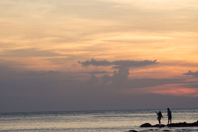 Silhouette people on beach against sky during sunset