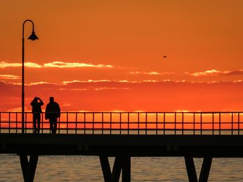 Silhouette man standing on railing against sea during sunset