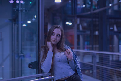 Young woman looking away while standing by railing at night