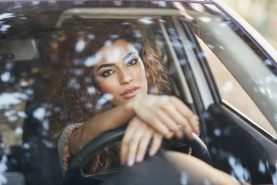 Portrait of young woman seen through car windshield