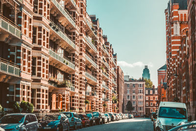 Cars parked on road by residential buildings in city against sky