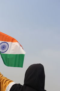 Rear view of person holding flag against sky