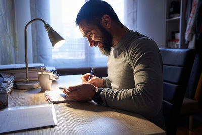 Young white man with a neat beard studying and looking at the phone at his desk