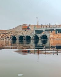 Arch bridge over river by buildings against sky