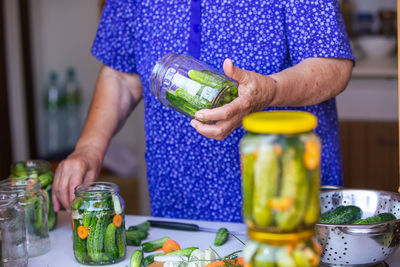 Process of canning a cucumber, senior woman canning fresh cucumbers with onion and carrots