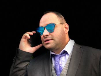 Close-up of businessman in sunglasses talking on mobile phone against black background