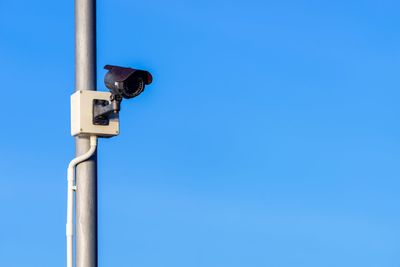 Low angle view of security camera against clear blue sky