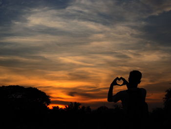 Silhouette man making heart shape against sky during sunset