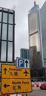 Road sign by modern buildings in city against sky