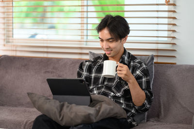 Young woman using phone while sitting on sofa at home