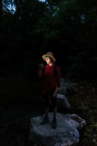 Female tourist standing on rock in woods at night and searching for route while using digital map on cellphone