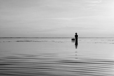 Silhouette man standing in sea against sky