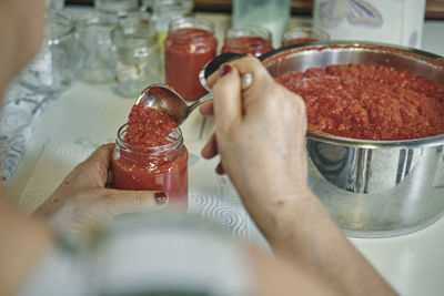 Cropped hands of woman filling food in jar on table