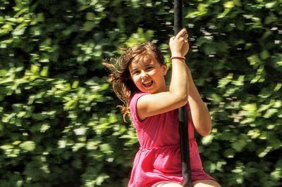 Portrait of happy girl on swing against trees