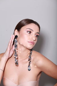 Indoor head shot of brunette model wearing long shiny earrings, professional make up tied hairstyle