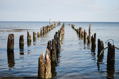 Wooden posts in sea against sky