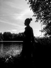 Rear view of silhouette woman looking at lake against sky