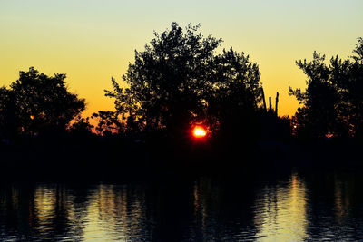 Silhouette trees by lake against sky during sunset