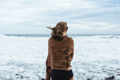 Rear view of woman standing at beach against sky