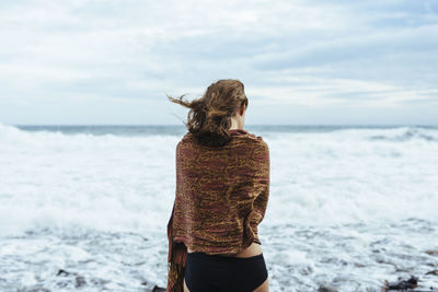 Rear view of woman standing at beach against sky