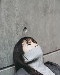 Close-up of young woman covering mouth with turtleneck against wall