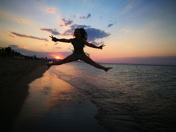 Silhouette woman jumping against sea during sunset