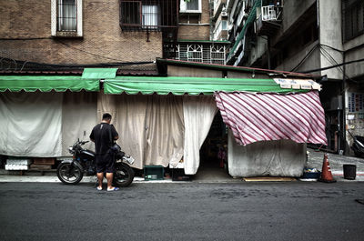 Rear view of man standing by motorcycle against buildings in city