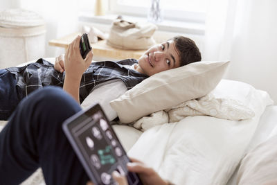 Brothers lying on bed and using phone and tablet