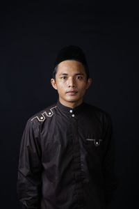 Portrait of young man standing against black background