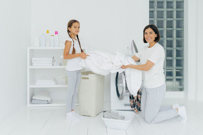 Portrait of smiling mother with daughter washing clothes in machine at home