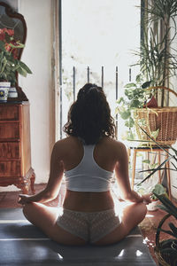 Rear view of seductive woman meditating while sitting at home