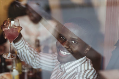Portrait of smiling young man with wineglass seen through glass of restaurant