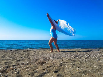 Full length of girl standing at beach against blue sky