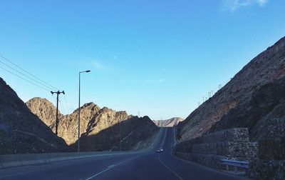 Road leading towards mountains against blue sky