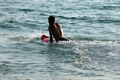 Rear view of shirtless man surfing in sea