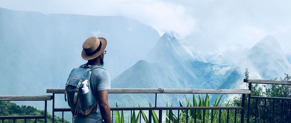 Rear view of man standing on railing against mountain