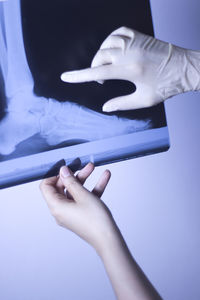 Cropped hands of woman holding x-ray image against wall