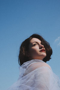 Low angle view of young woman in white dress against sky
