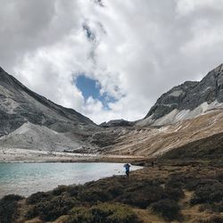 Man standing on mountain by lake against sky