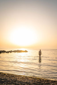 Silhouette person in sea against sky during sunset