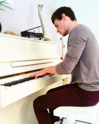 Side view of young man playing piano at home