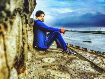 Side view of boy sitting on shore against sky